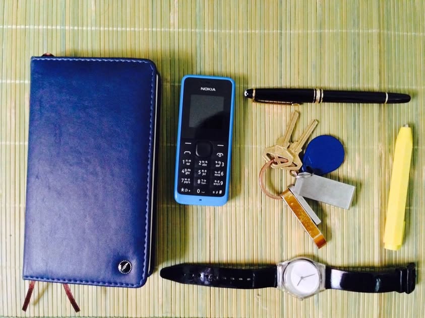 Everything carried for three years of fieldwork laid out on a bamboo mat — a notebook, a dumb phone, a fountain pen, keys, a watch
